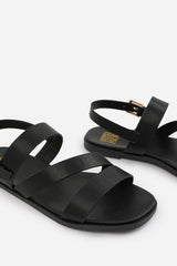 NESSA WIDE FIT FLAT SANDALS WITH CROSS OVER STRAP AND BUCKLE CLOSURE IN BLACK FAUX LEATHER