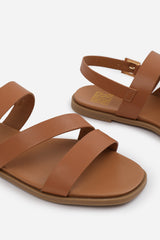 NESSA FLAT SANDALS WITH CROSS OVER STRAP AND BUCKLE CLOSURE IN TAN FAUX LEATHER